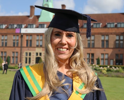 Emma Ellis wearing a graduation cap and gown, standing in front of the HCA Building at Hope Park.